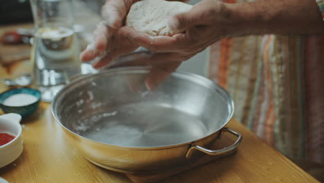 las manos del chef amassando la masa en un cuenco de metal para cocinar en la cocina