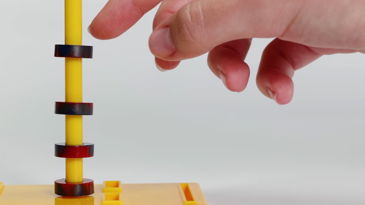 Close-up of hands manipulating magnetic rings on a yellow rod, demonstrating magnetic interactions.