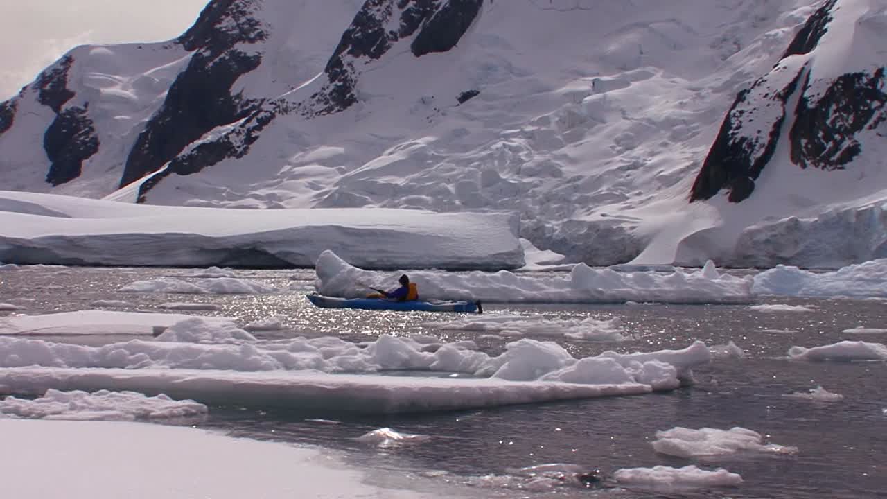 한 남자가 광활한 빙원과 빙하 근처의 북극 또는 남극 지역을 통해 카약을 노로 젓습니다.