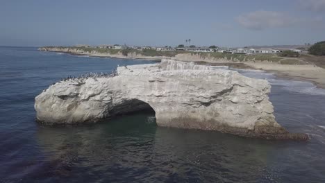 aerial drone shot of rock formation archway and wildlife birds