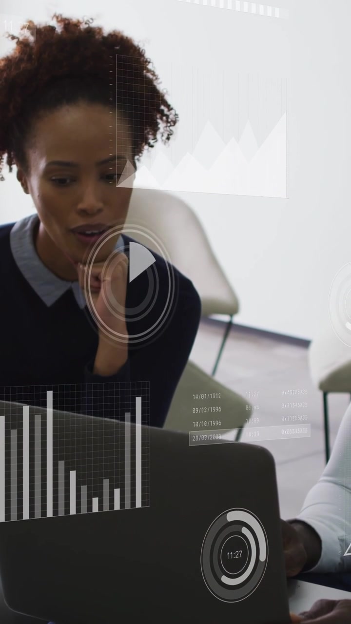 Vertical video: Woman scanning laptop while man tilting device, live charts updating for business