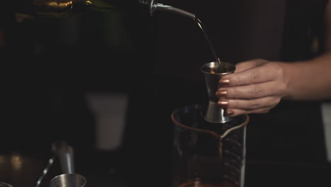 bartender measures whiskey using jigger and pours into glass, slow motion