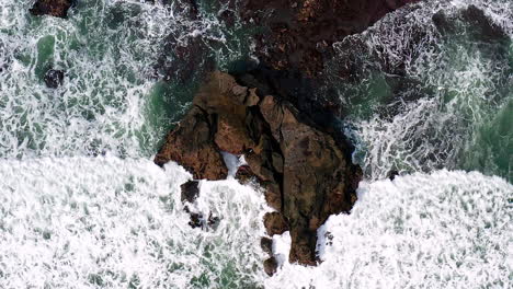 Sharp-jagged-rock-on-rugged-coastline-washed-by-big-foamy-sea-wave