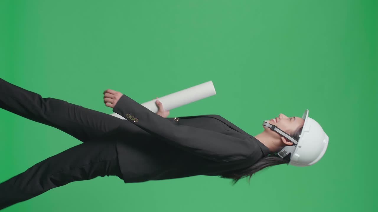 Side View Of Smiling Asian Female Engineer With Safety Helmet And Blueprint Walking In The Green Screen Studio