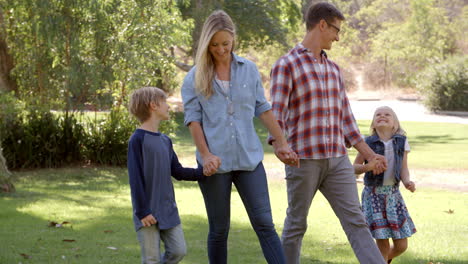 young family walk holding hands in a park in the sun, pan