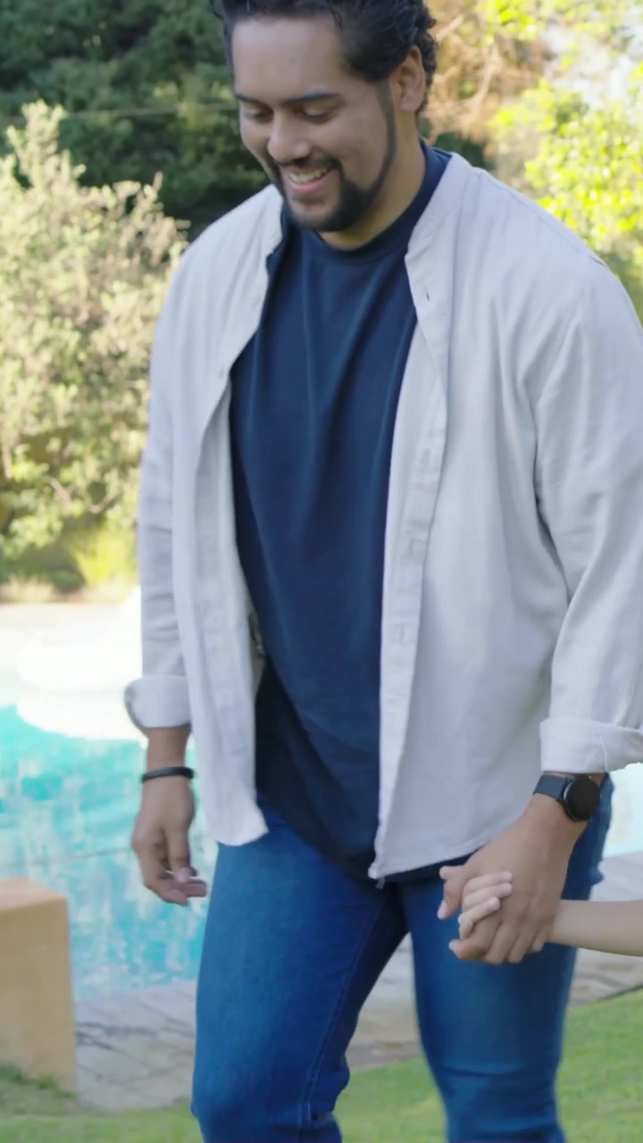 Video verticale: Bambino che si allunga, papà con camicia aperta che guida il bambino lungo la piscina in giardino per sicurezza.
