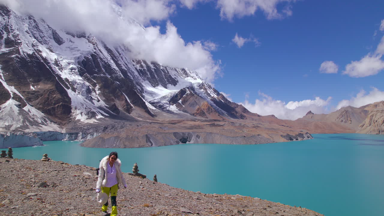 Tilicho Lake Manang Nepal, female tourist treks World's Highest Altitude Lake, Annapurna Mountain landscape drone shot, clouds, snows, nature, sunny weather, blue lake 4K