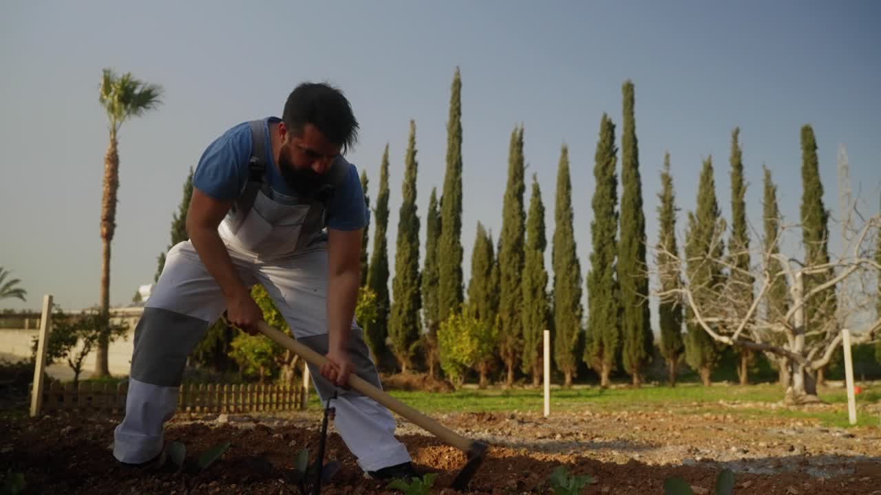 Vue large d'un homme labourant le sol dans son jardin.