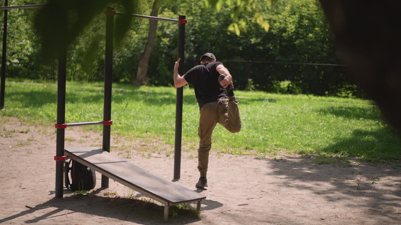 Male Practicing Singleleg Balance Outdoors, Standing On One Leg With Aid Outdoors, Male Individual Performs Controlled Singleleg Stance With Support On Bright Sunny Afternoon Outdoors