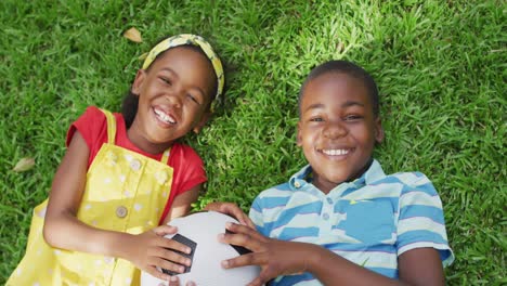 Animation-of-happy-african-american-siblings-lying-on-lawn-and-holding-ball
