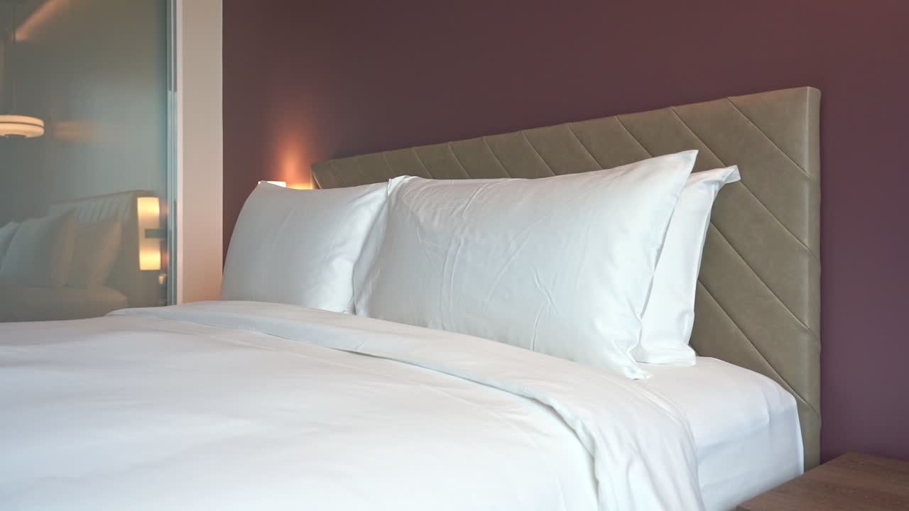 Kingsize bed in cozy hotel bedroom, white sheets and pillows, pan left