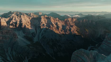 Pushing-in-drone-shot-of-the-breathtaking-Dolomite-peaks-in-Italy-at-sunrise,-with-a-snowy-foreground-slope-and-valley-leading-to-the-mountains