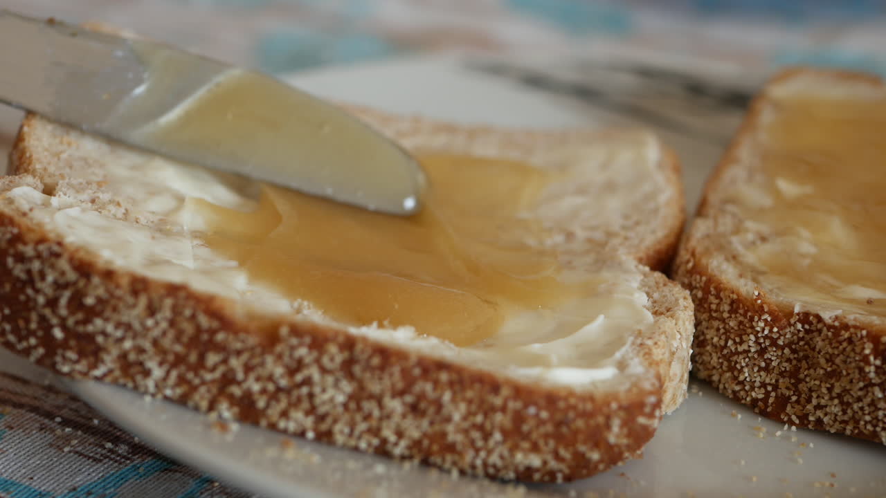 Delicious yellow honey being spread by silver knife on bread and butter