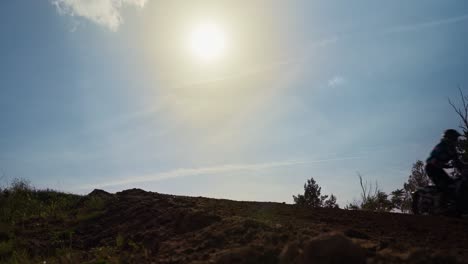 Low-angle-shot-of-cross-motor-bikes-jumping-over-a-hillock-while-driving-along-on-a-suuny-day