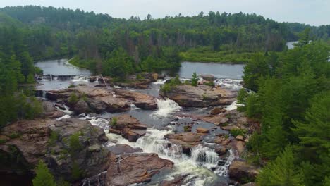 Aerial-View-River-Flowing-To-The-Waterfall-Within-The-Dense-Forest-In-Daytime