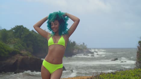 mujer joven de pie en un acantilado en un bikini amarillo con olas del océano en el fondo