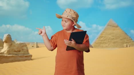 asian boy with a hat using a tablet then smiling and pointing to side while traveling in giza pyramid. boy researcher examines something, travel tourism adventure concept