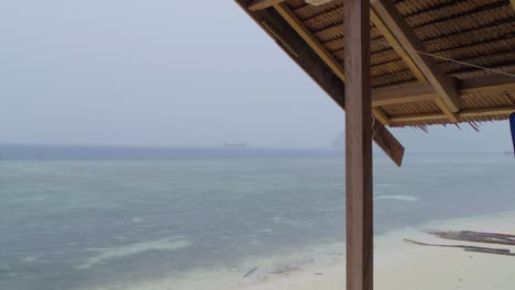 the-tropical-heavy-rain-seen-from-a-hut-on-Kri-Island-in-the-Raja-Ampat-Archipelago,-gazing-out-onto-the-vast-sea-as-rain-cascades-from-the-sky