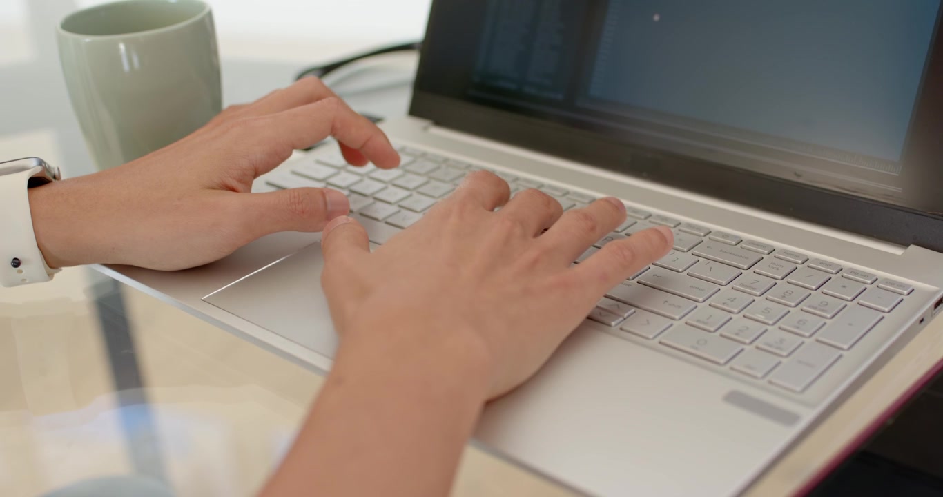 Homem asiático iniciando tarefa, digitando constantemente em laptop prateado em mesa de escritório em casa com pulseira branca.