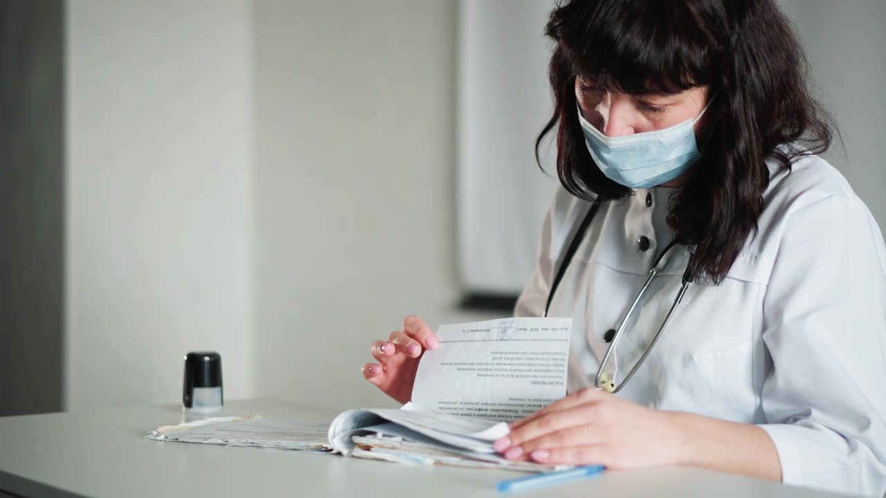 Médico blanco en el escritorio documentando notas de consulta, médico enmascarado revisa el historial y escribe observaciones, estetoscopio sobre la mesa, iluminación de consultorio clínico, postura atenta y mano cuidadosa
