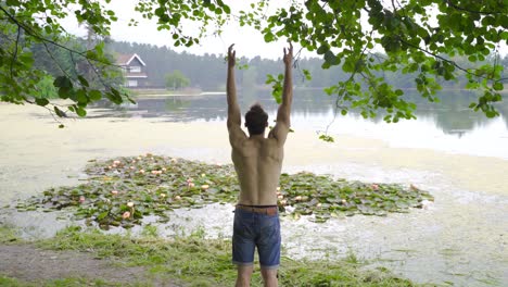 joven levantando felizmente sus manos junto al lago.