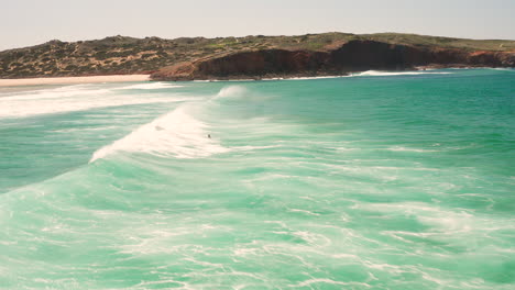 Aerial:-Surfing-the-beach-of-Bordeira-in-the-Algarve,-Portugal