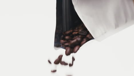 roasted coffee beans falling down from metallic noname coffee bag in front of white background