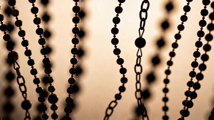 Swaying hanging ball-chains and oval-link metal chains drifting from studio window breeze, backlit