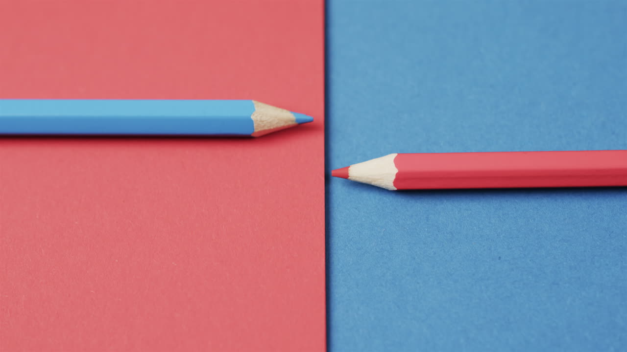 Overhead view of blue and red crayons arranged on red and blue background, in slow motion