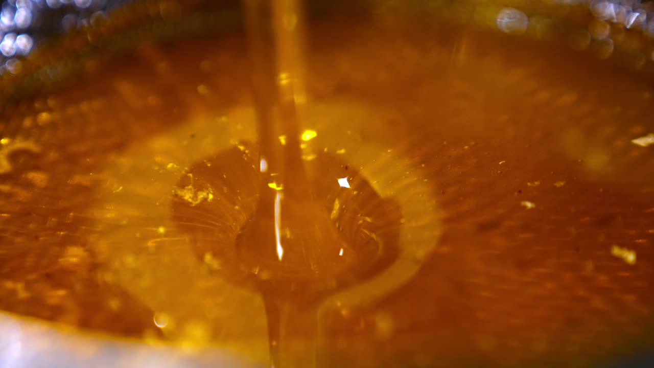 Flow of yellow fresh honey falling into the bowl. Delicious natural healthy organic product after the extraction. Close up.