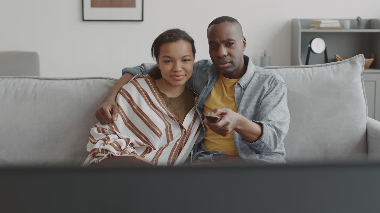 Coppia multietnica guarda la TV e si abbraccia