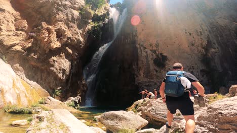 hiker admiring a waterfall and natural pool in a rocky landscape