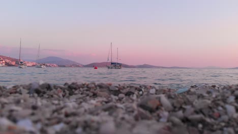 Low-angle-view-of-rocky-beach-with-yachts-and-beautiful-pink-sky