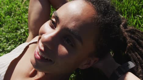 close up of african american woman lying on grass and smiling in park