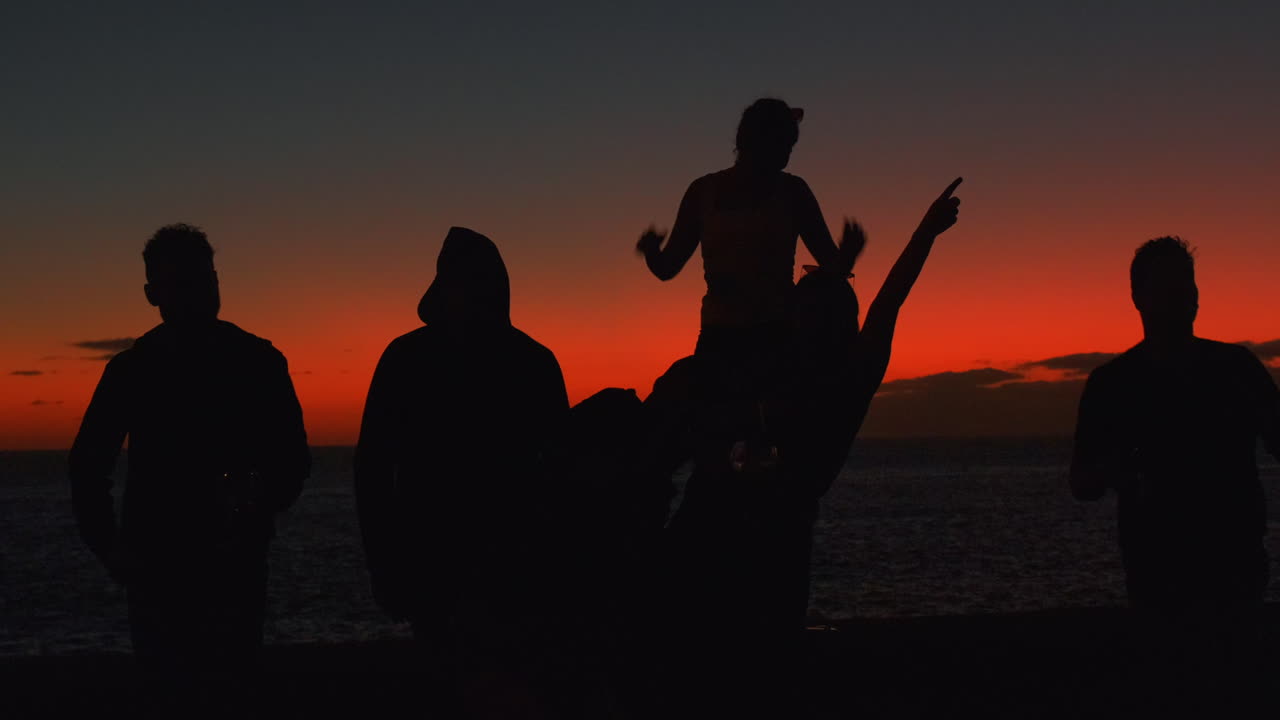 Dark Silhouette showing group of young people celebrating outdoors and enjoying red colored sunset in background