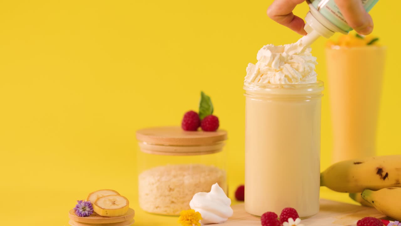 Frullato di banana con panna montata in uno studio luminoso, circondato da frutta fresca e dessert