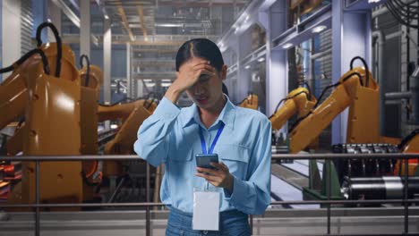 asian female with her smarphone with industrial robotic arms working, she is nodding her shead with dissapionted
