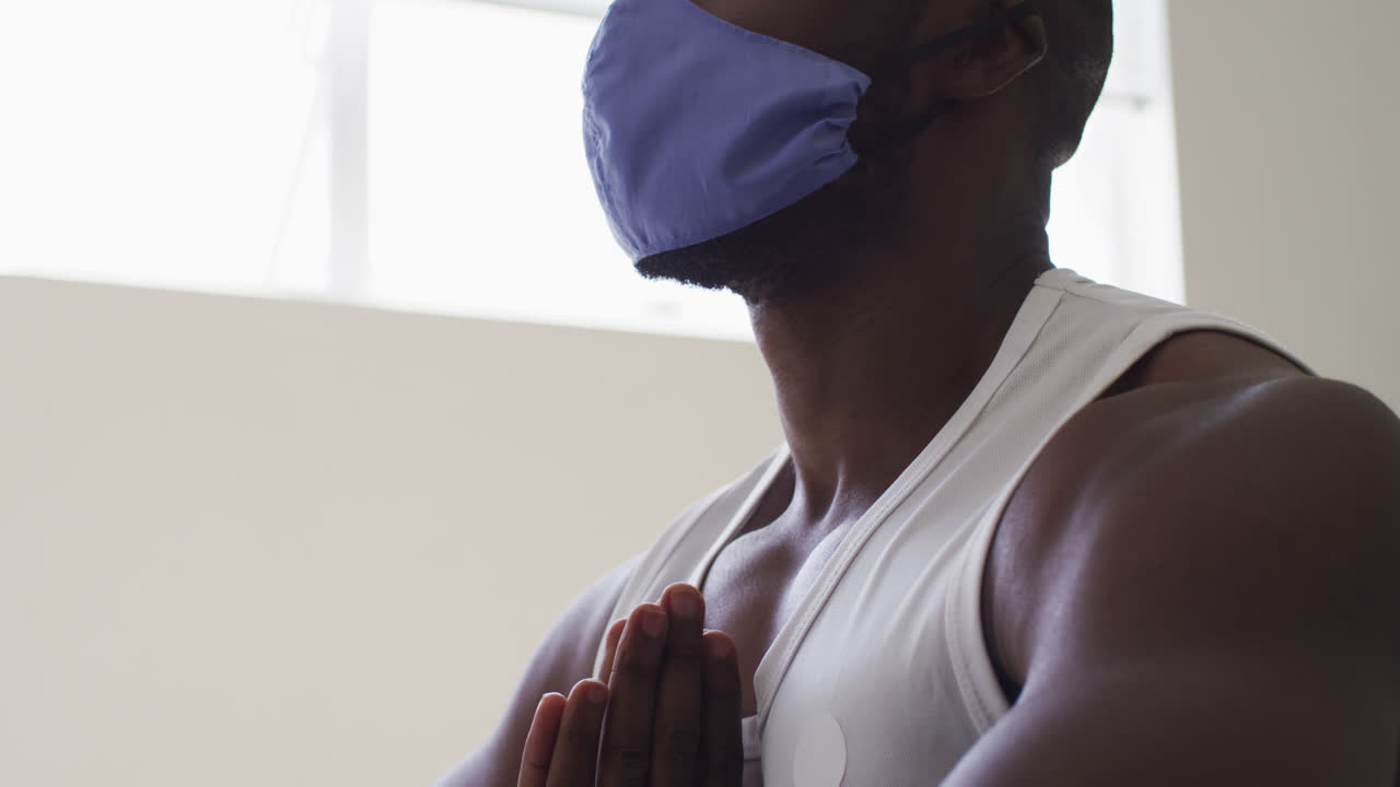 Uomo afroamericano in forma che indossa una mascherina e pratica yoga in uno studio di yoga