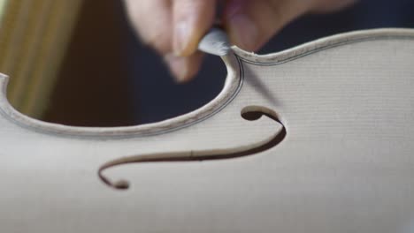 macro close up of artisan luthier maker work on new classic handmade raw violin smooth edge in waist and purfling rasp in workbench of workshop in cremona italy 4k video