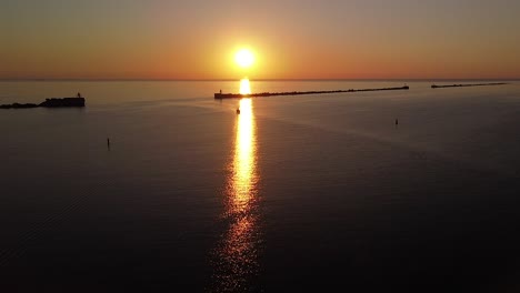 hermosa puesta de sol vibrante aérea de alto contraste sobre el tranquilo mar báltico, muelle de roca en el puerto de liepaja , barco de vela distante, disparo de drones de gran angular avanzando