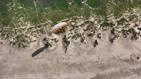 paraglider sailing alone low above ouddorp waterfront sand dunes