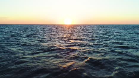 dolly inversa aérea sobre el océano abierto retirándose hacia atrás, puesta de sol brillo dorado a través del océano