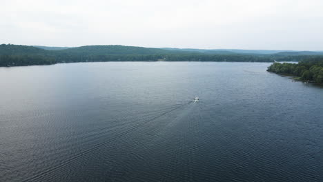 Aerial-pullback-away-from-boat-driving-out-into-lake,-epic-view-of-large-v-wake