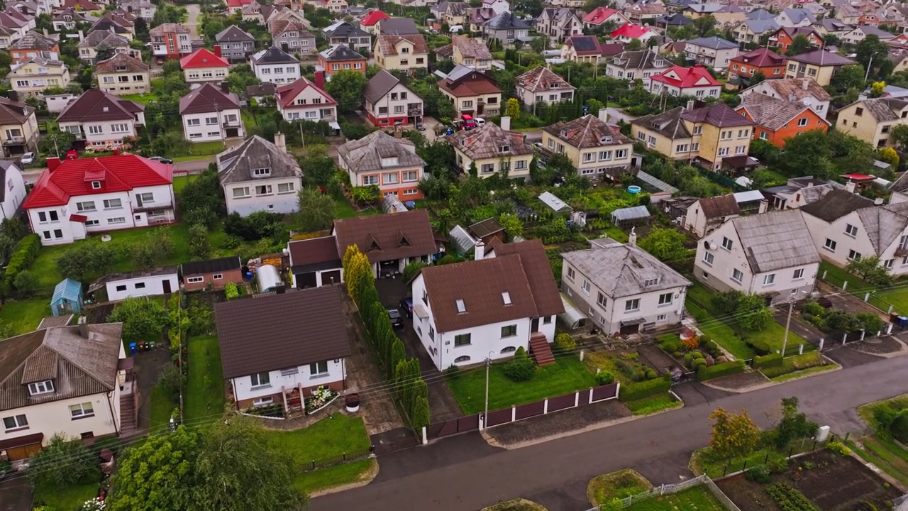 Drone terbang maju di atas rumah-rumah pinggiran kota dan halaman hijau Siauliai, Lituania.