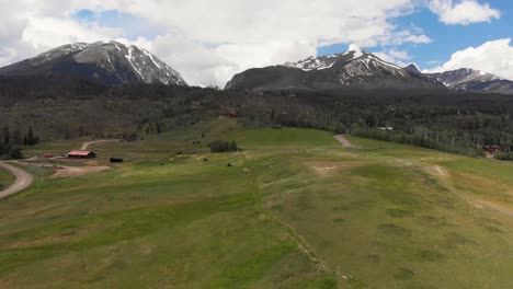 Snow-covered-rocky-mountains-and-open-country-hillside-fly-over-tall-grass-during-the-spring