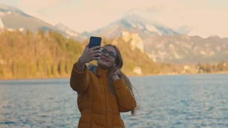 Vídeo-De-4k-De-Una-Hermosa-Joven-Caucásica-Tomando-Una-Foto-Selfie-En-Un-Destino-Turístico-Muy-Famoso-Bled,-Eslovenia