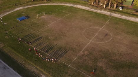 Aerial-shot-of-trainer-couch-talking-to-football-team-on-dried-amateur-soccer-field