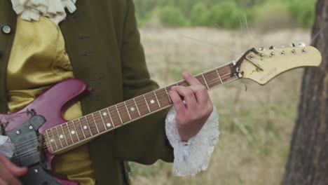 person in historical costume playing a vintage guitar by a river