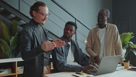 team of male colleagues discussing business plan on laptop in office
