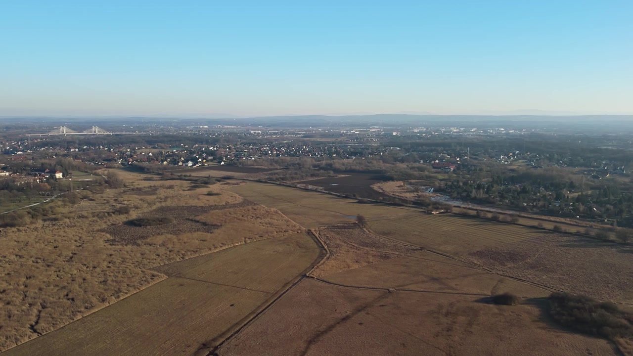 Łąki Nowohuckie a Cracovia presenta un'ampia distesa di prati e zone umide che confina con case suburbane e infrastrutture sotto un cielo diurno sereno, catturato in una vista aerea